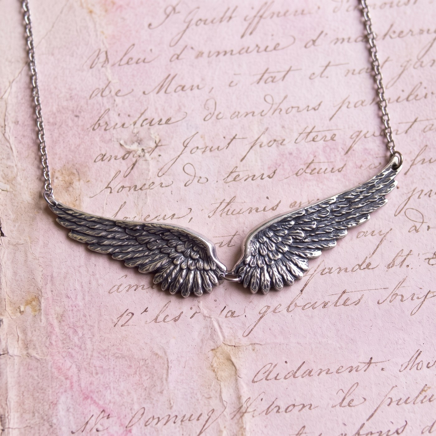 Antiqued silver angel wing necklace on pink script paper